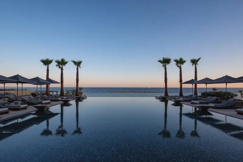 Infinity-edge pool with palms and parasols at sunset over the sea