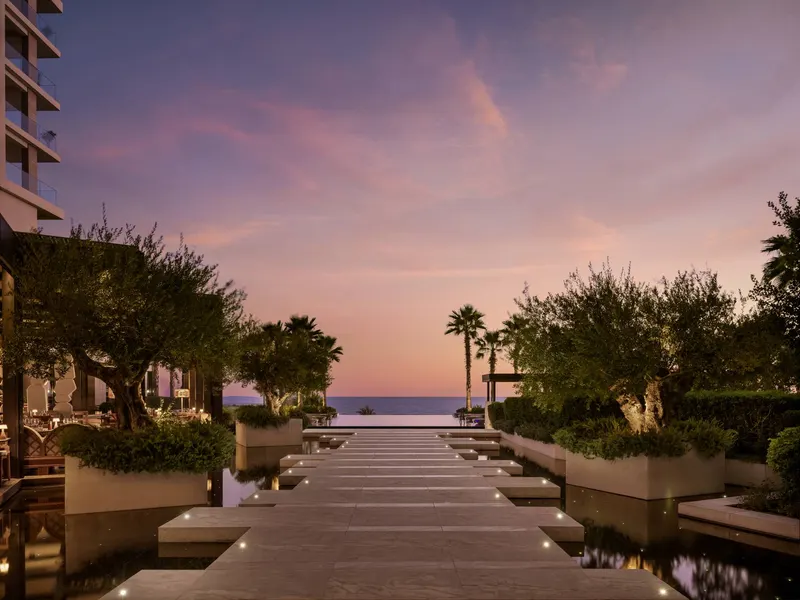 Lit garden walkway leading towards the sea at dusk