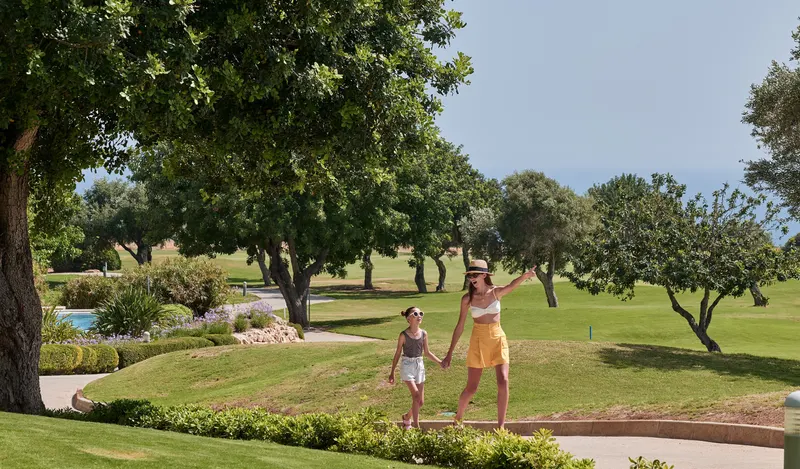Mother and child walking across the resort lawns under olive trees