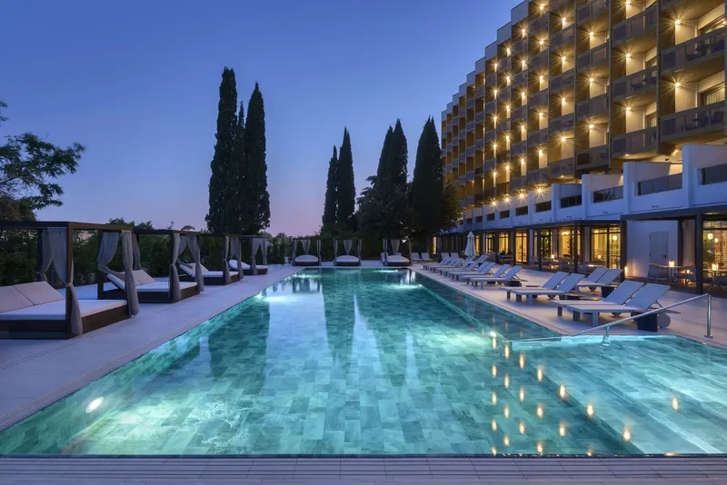 Outdoor pool at dusk with cabanas and the illuminated hotel facade