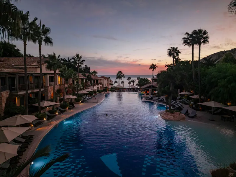 Long lagoon pool lined with palms and parasols at dusk