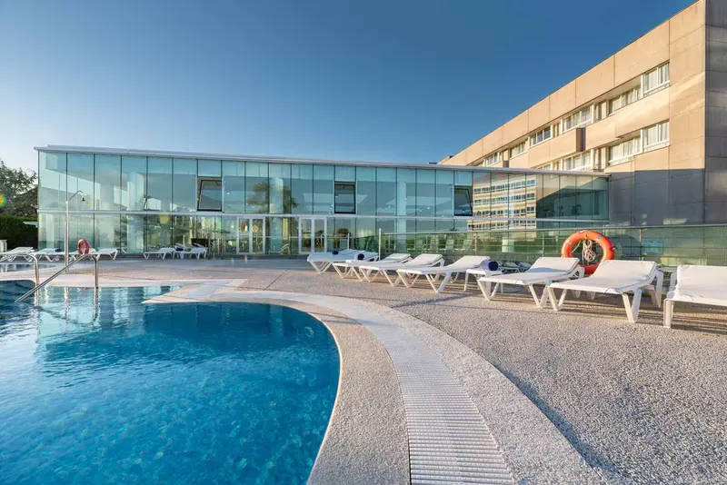 Curved outdoor pool with loungers by the glass spa building