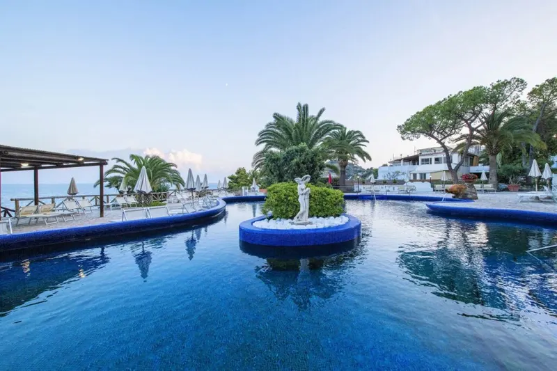 Blue thermal pool with a statue island, terrace and sea at dusk