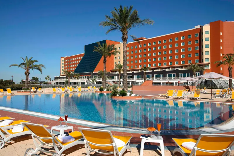 Pool with sunloungers and the hotel building behind palms
