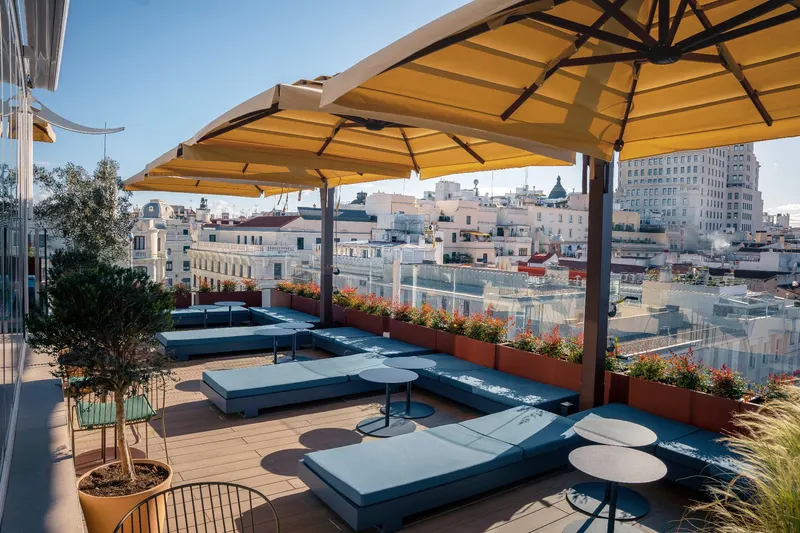 Rooftop loungers under yellow umbrellas with Gran Via views