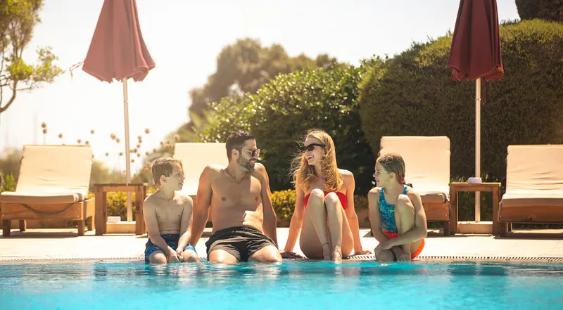 Family sitting at the pool edge with umbrellas behind